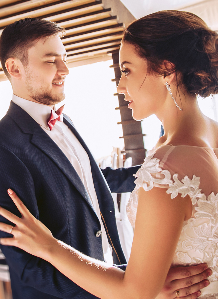 A bride in a lace gown and a groom in a navy suit smiling at each other during their first dance